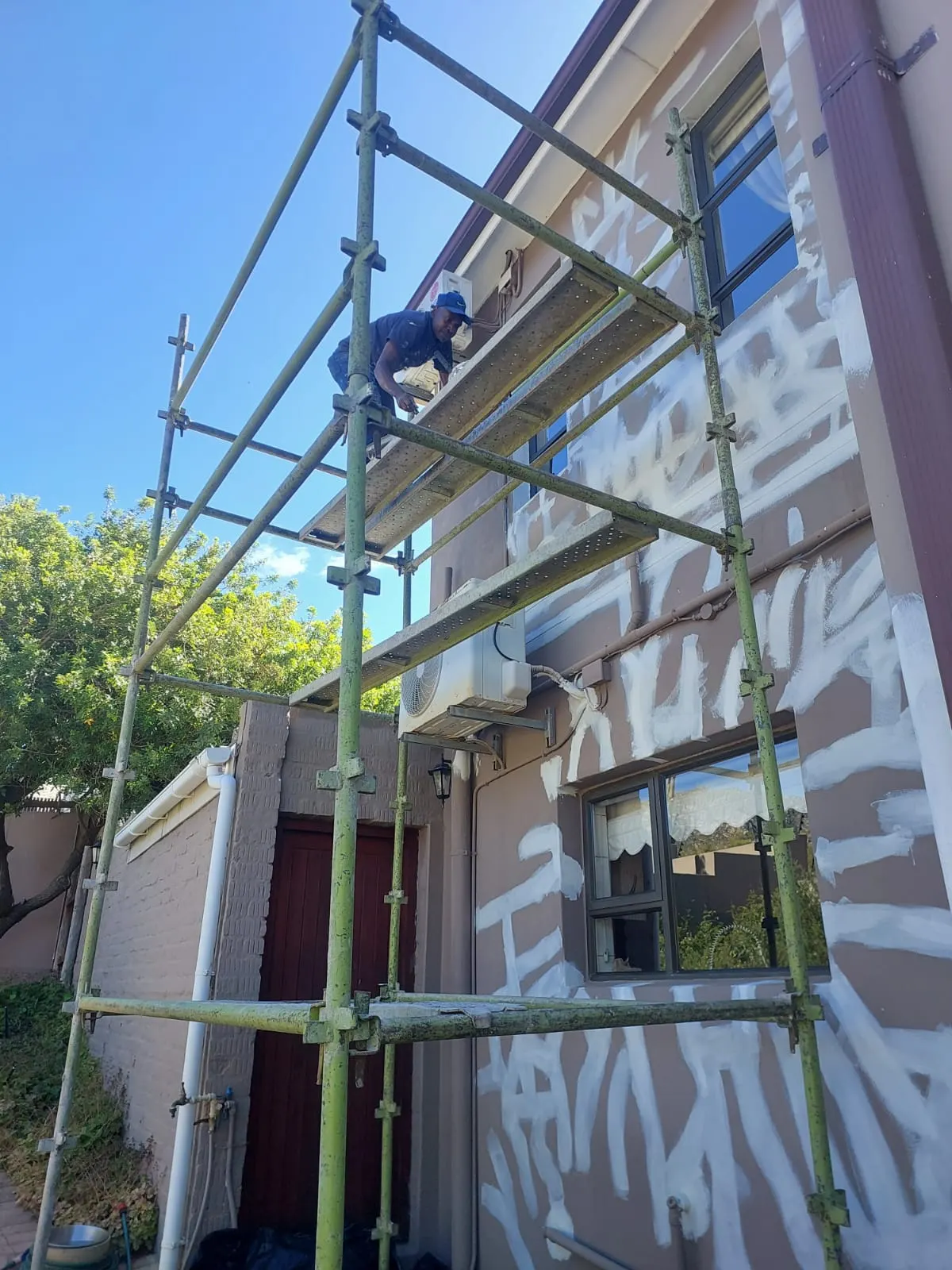 Painter on scaffolding patching wall cracks before exterior painting